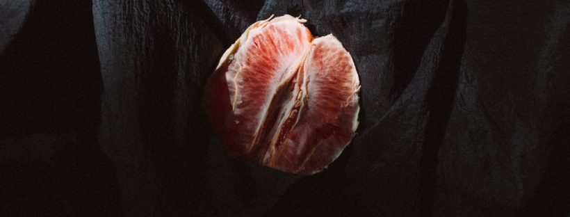 A blood orange, peeled and halved, lies partially covered on a wrinkled, black sheet.