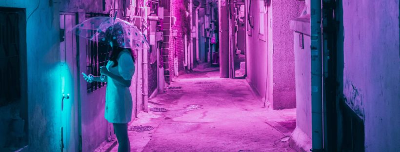 A woman carrying an umbrella attempts to enter a building through a neon-lit side entrance.