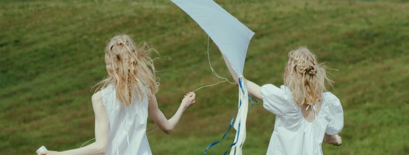 women in white dress playing with kite on the grass field